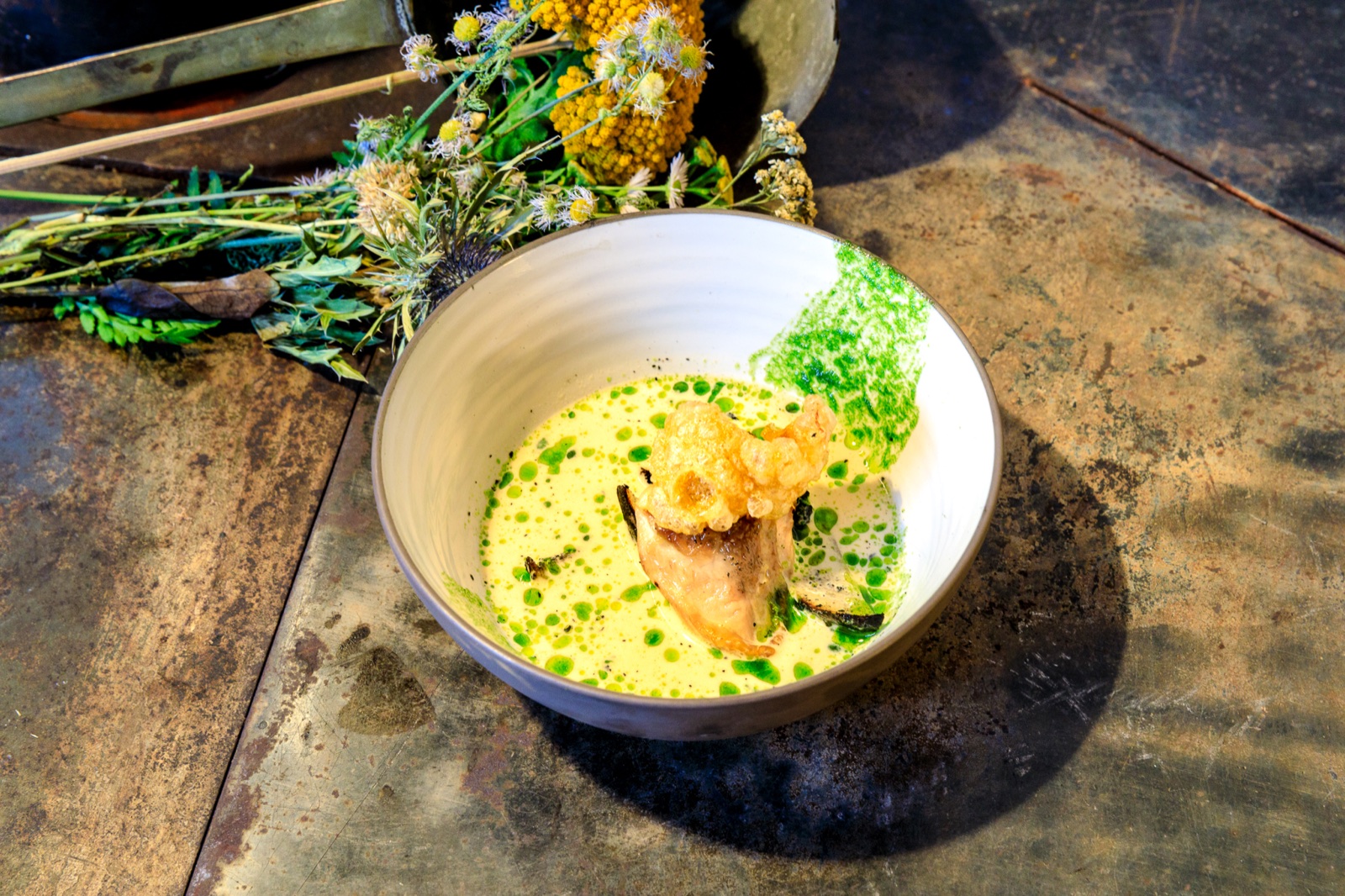 Ein angerichtetes Gericht mit Fisch, Kräuteröl und knusprigem Topping.